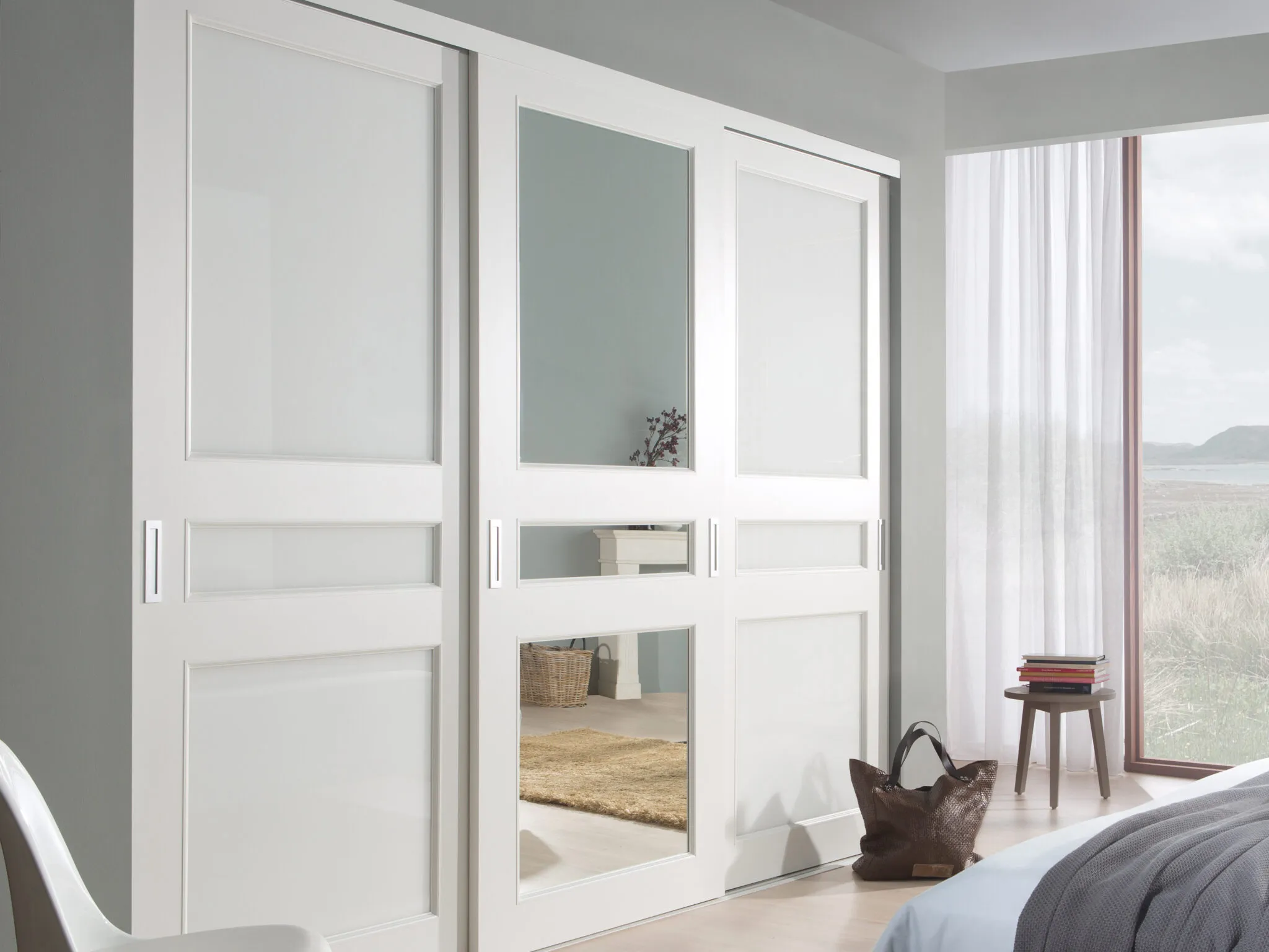 White framed sliding wardrobe doors with mirror panels in a bedroom by a window