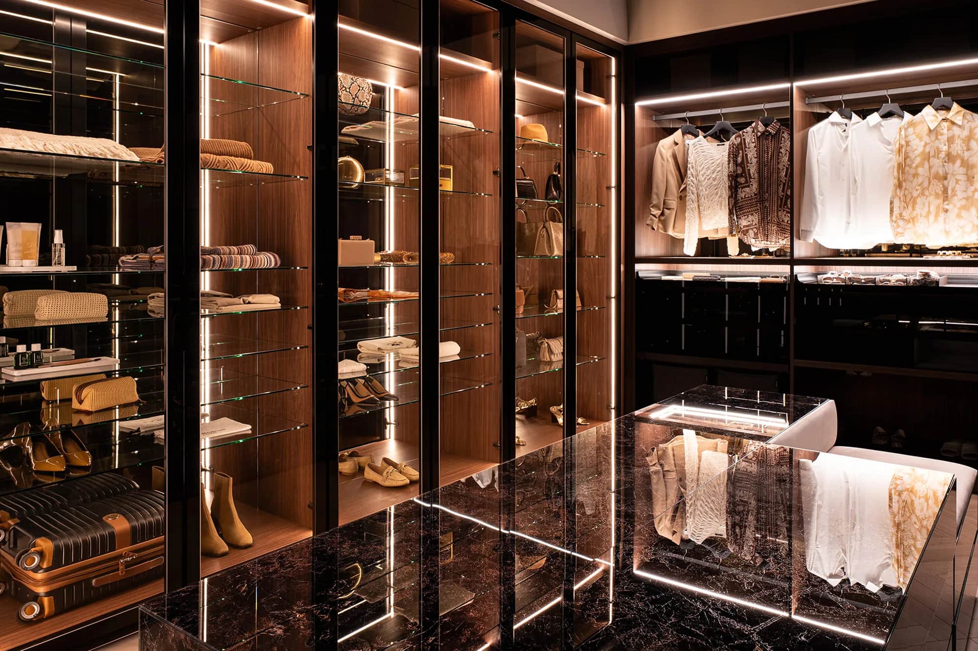 Dark walk-in dressing room with glass-fronted shelves, LED lighting and a marble-topped island