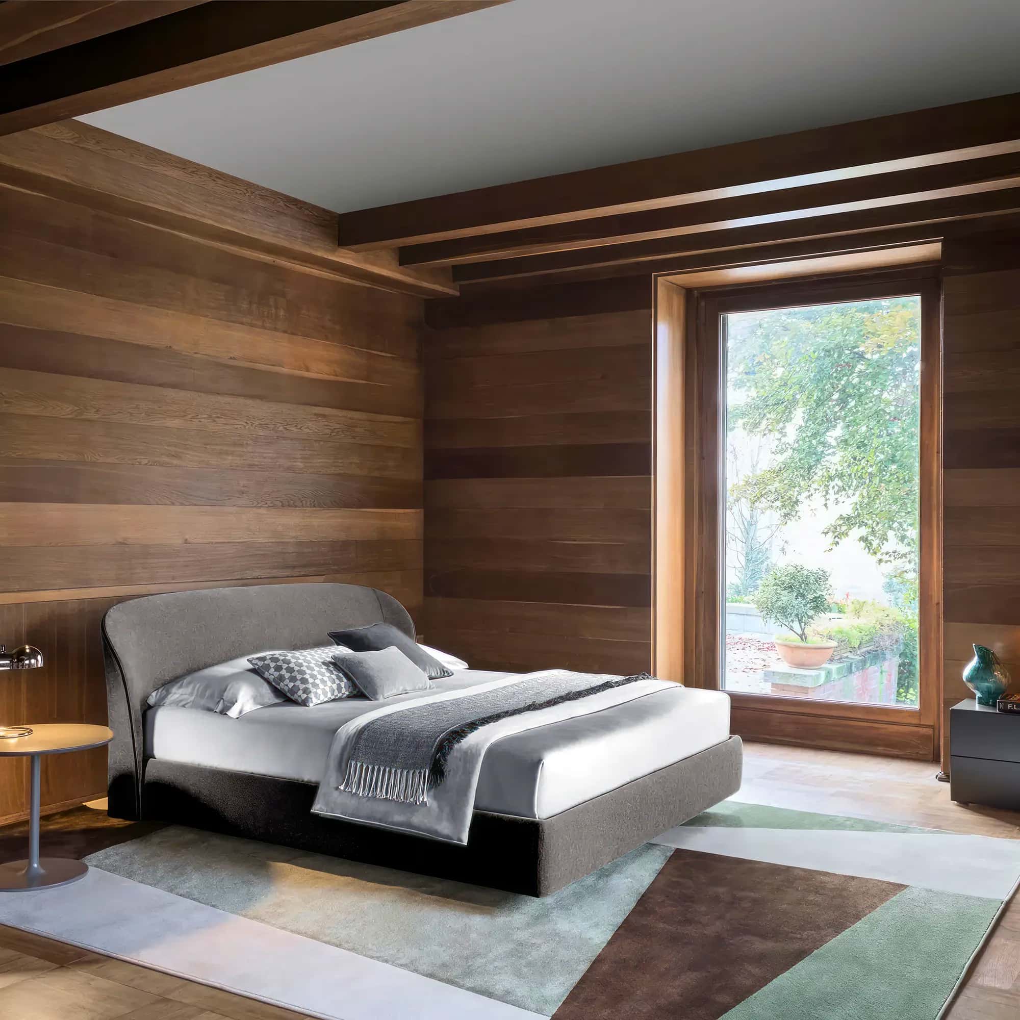 Upholstered bed in a bedroom with wood-panelled walls and a large window