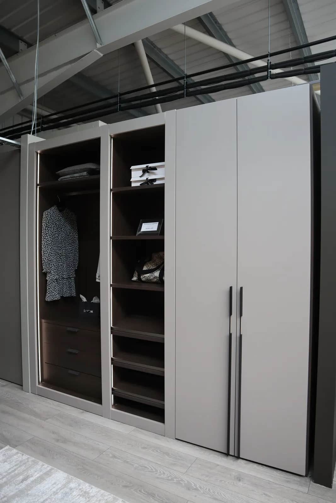 Taupe fitted wardrobe with open shelving, drawers and long dark vertical handles
