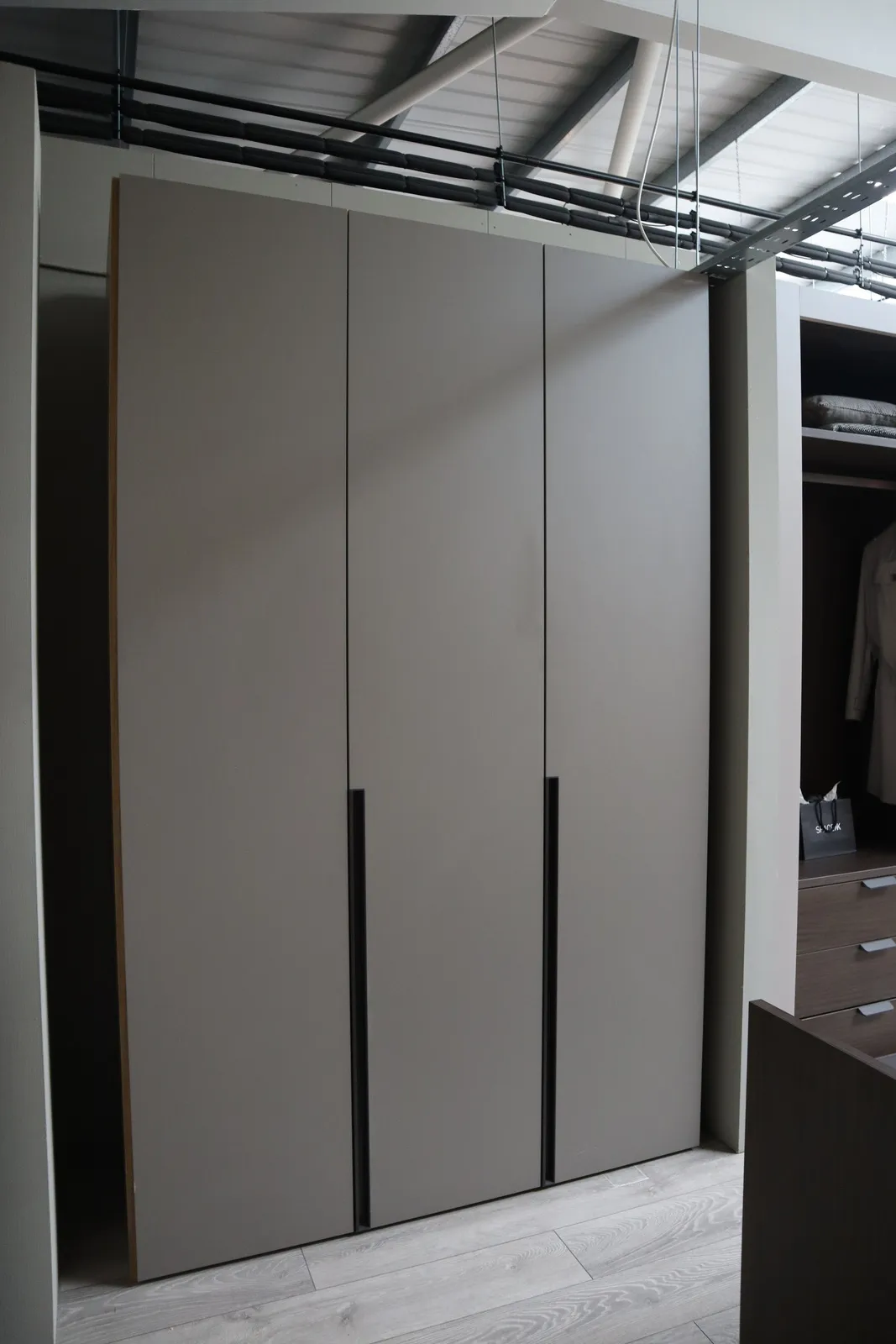 Three-door taupe fitted wardrobe with dark recessed vertical handles