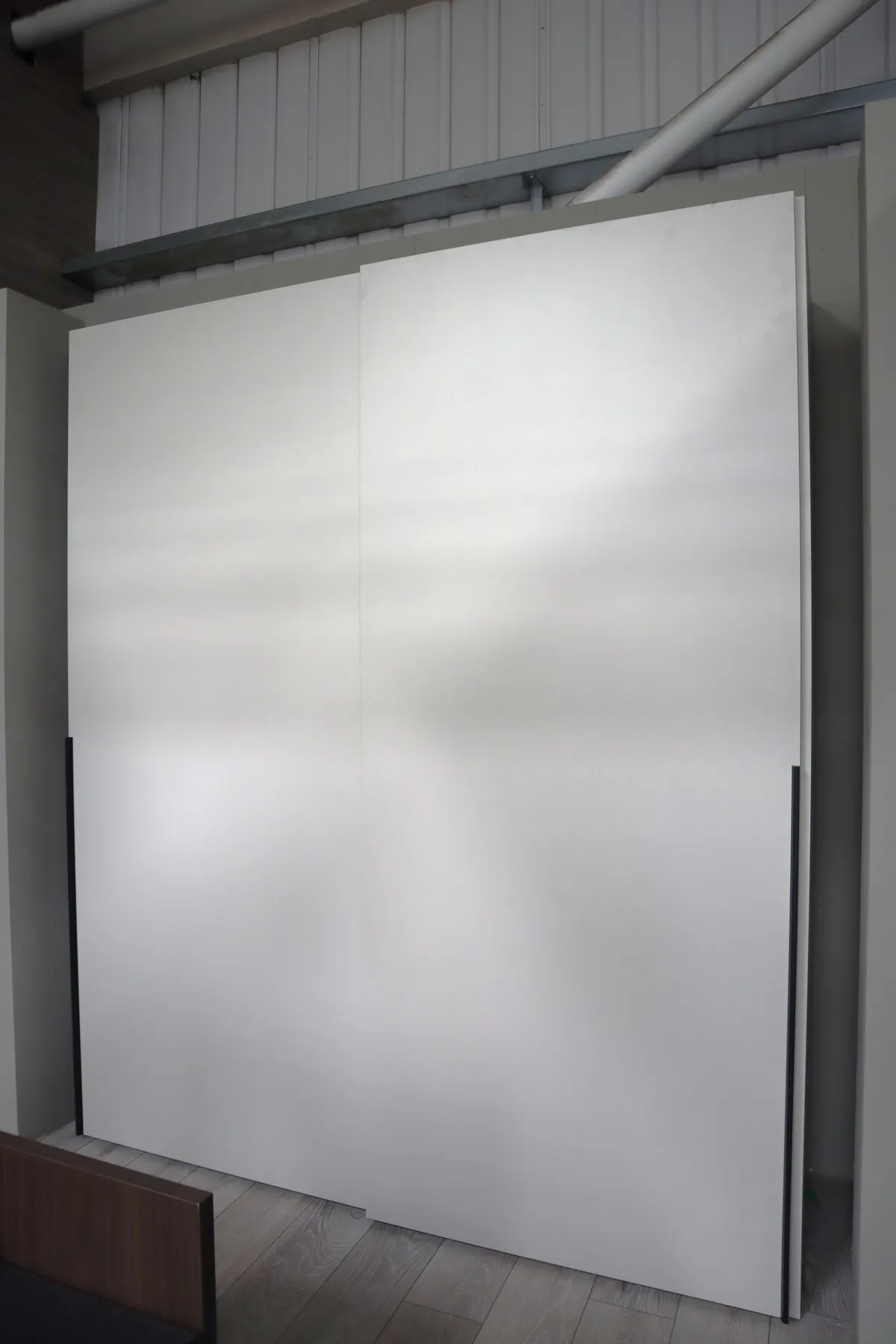 White sliding door wardrobe in a showroom with slim dark edge handles