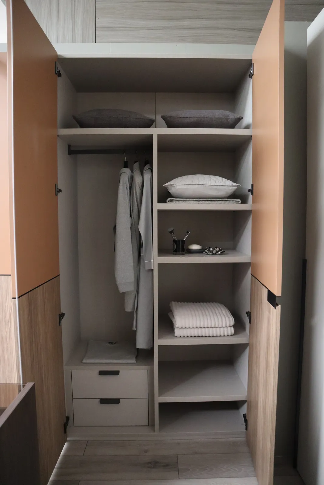 Wardrobe with tan and oak doors open to hanging robes, drawers and folded towels