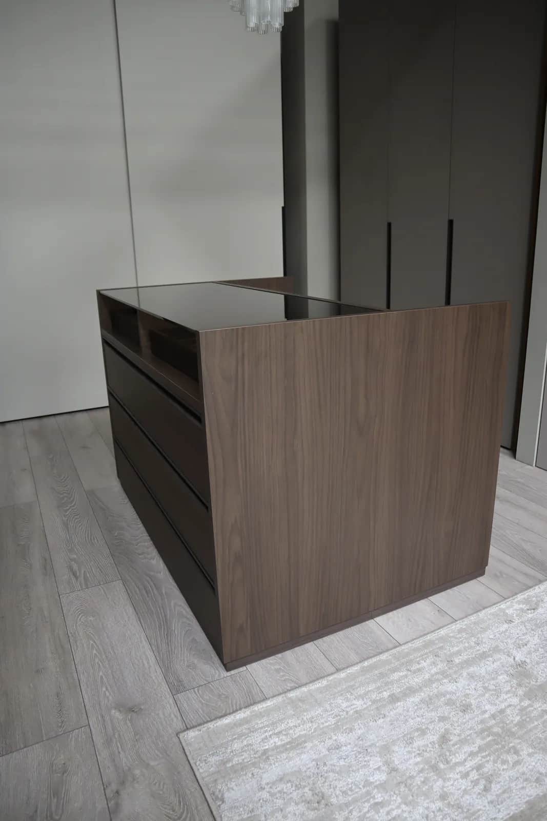 Walnut island unit with deep drawers and a dark glass top in a dressing room