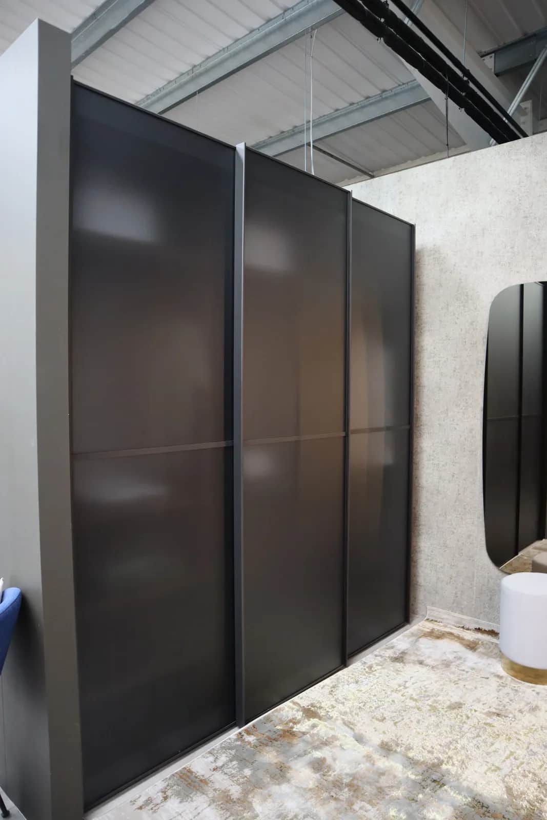 Three-door sliding wardrobe with smoked glass panels and dark frames in a showroom