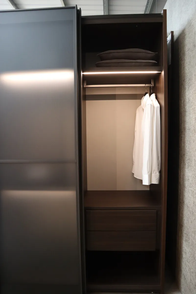 Dark wardrobe with smoked glass sliding door open to hanging shirt, shelf and drawers