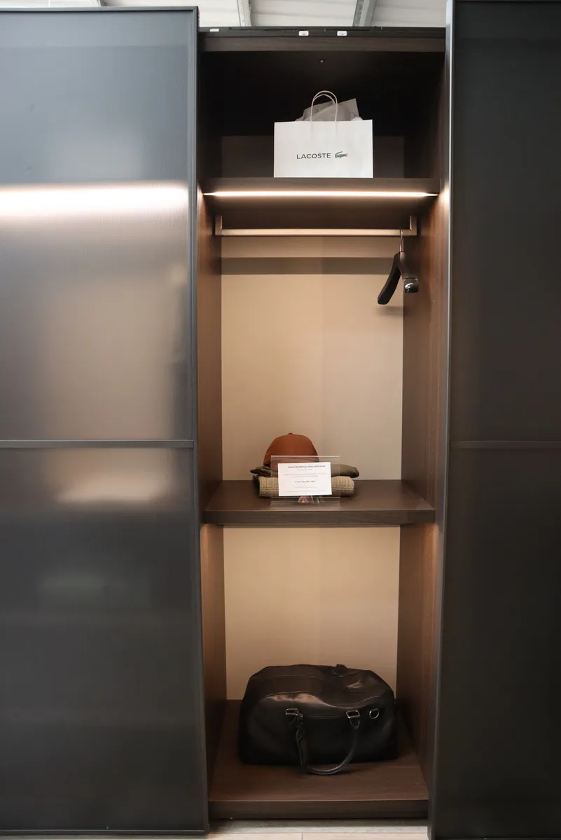 Smoked glass sliding wardrobe door open to LED lit shelves holding a bag and cap