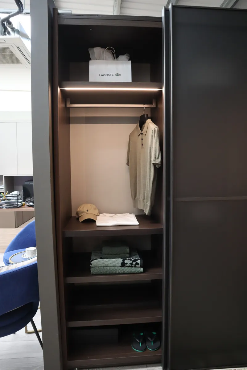 Open wardrobe with LED lit hanging rail, folded clothes and shelves beside smoked glass door