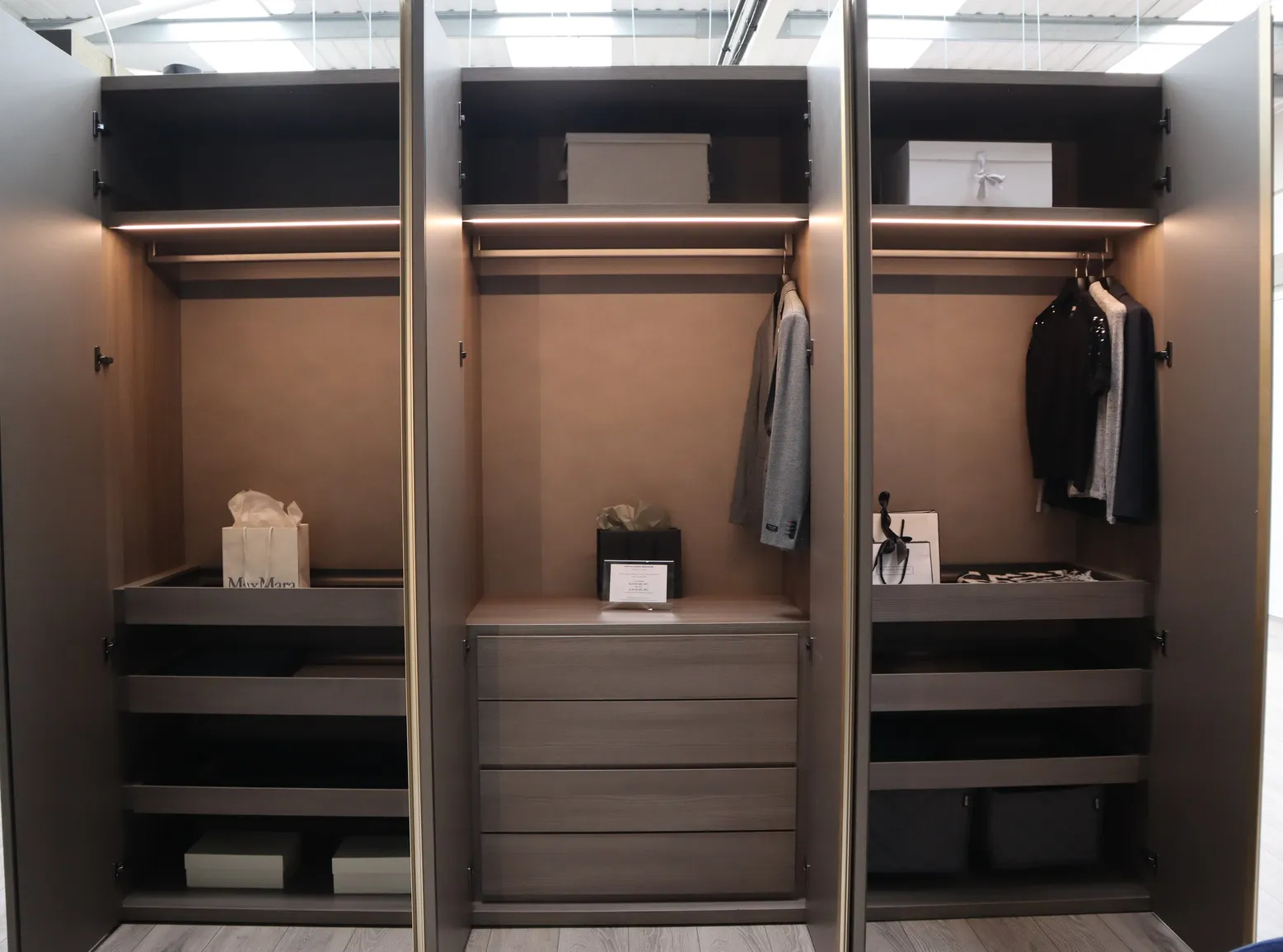 Open wardrobe doors showing LED lit hanging rails, drawers and shelves in dark bronze