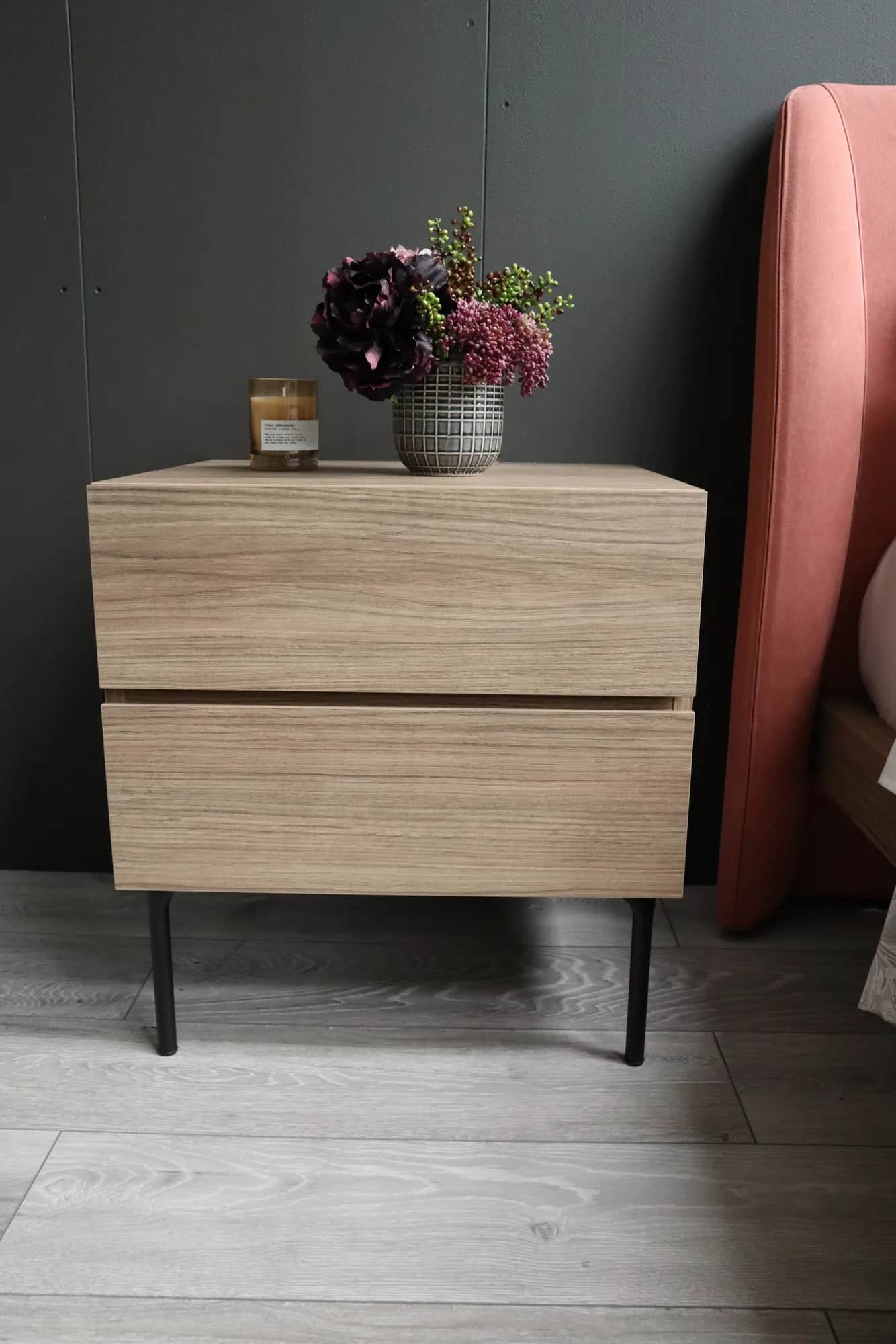 Oak-effect two-drawer bedside cabinet on black legs, with flowers and a candle