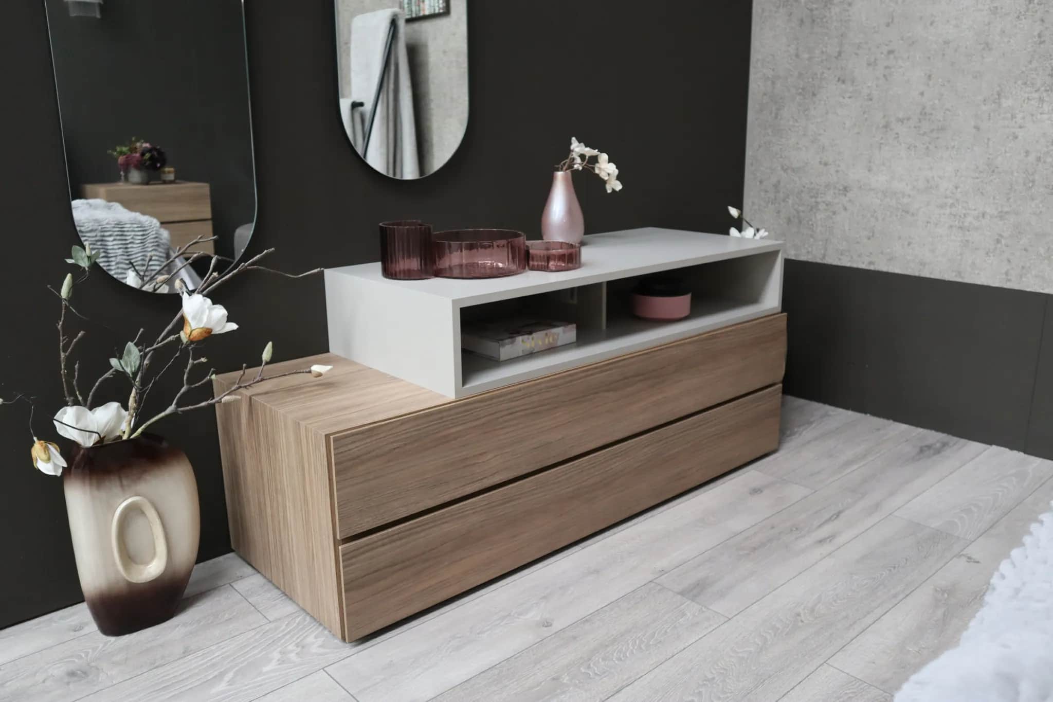 Walnut two-drawer chest with open grey shelf unit and a vase of flowers