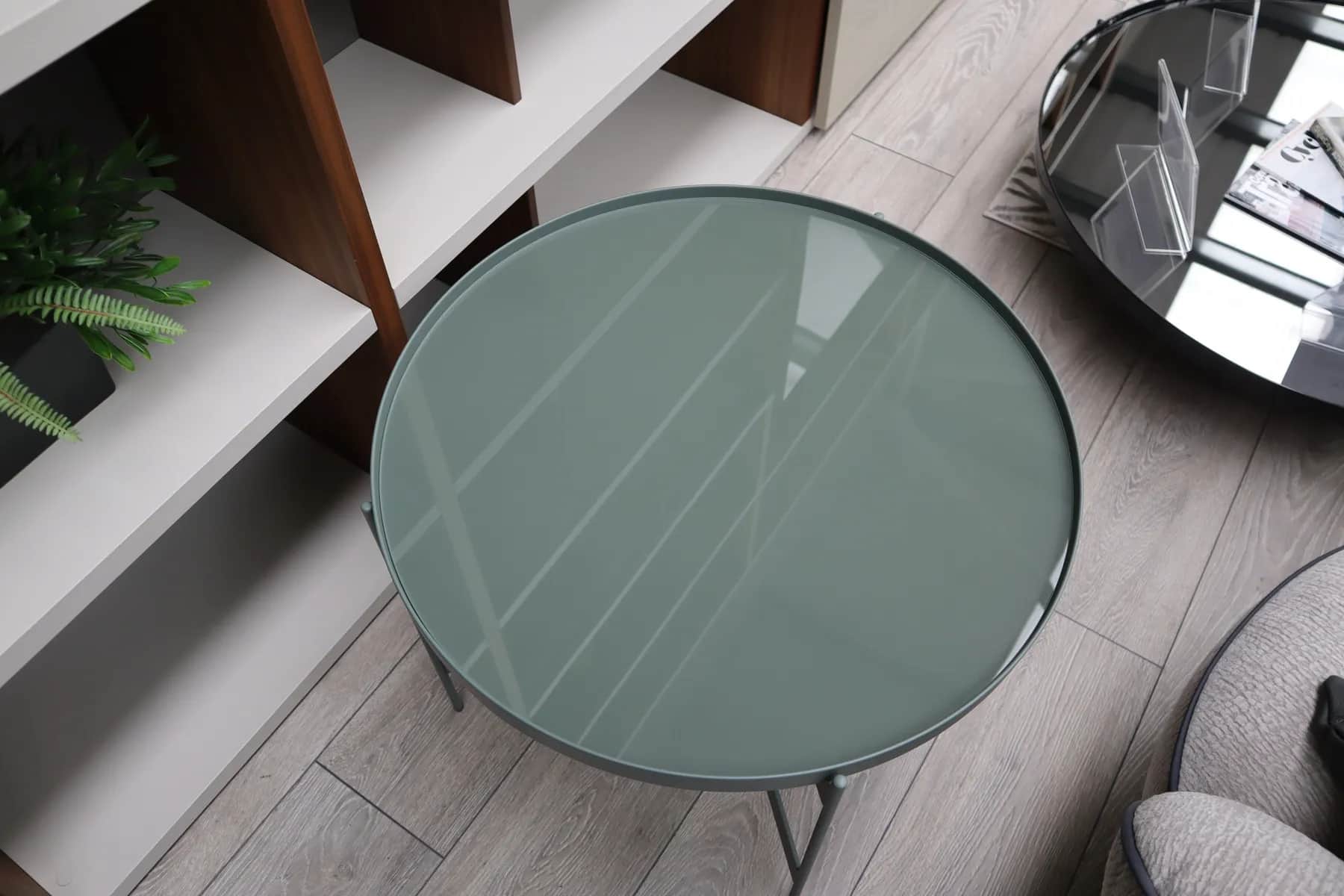Round sage green glass-topped side table seen from above beside walnut and grey shelving