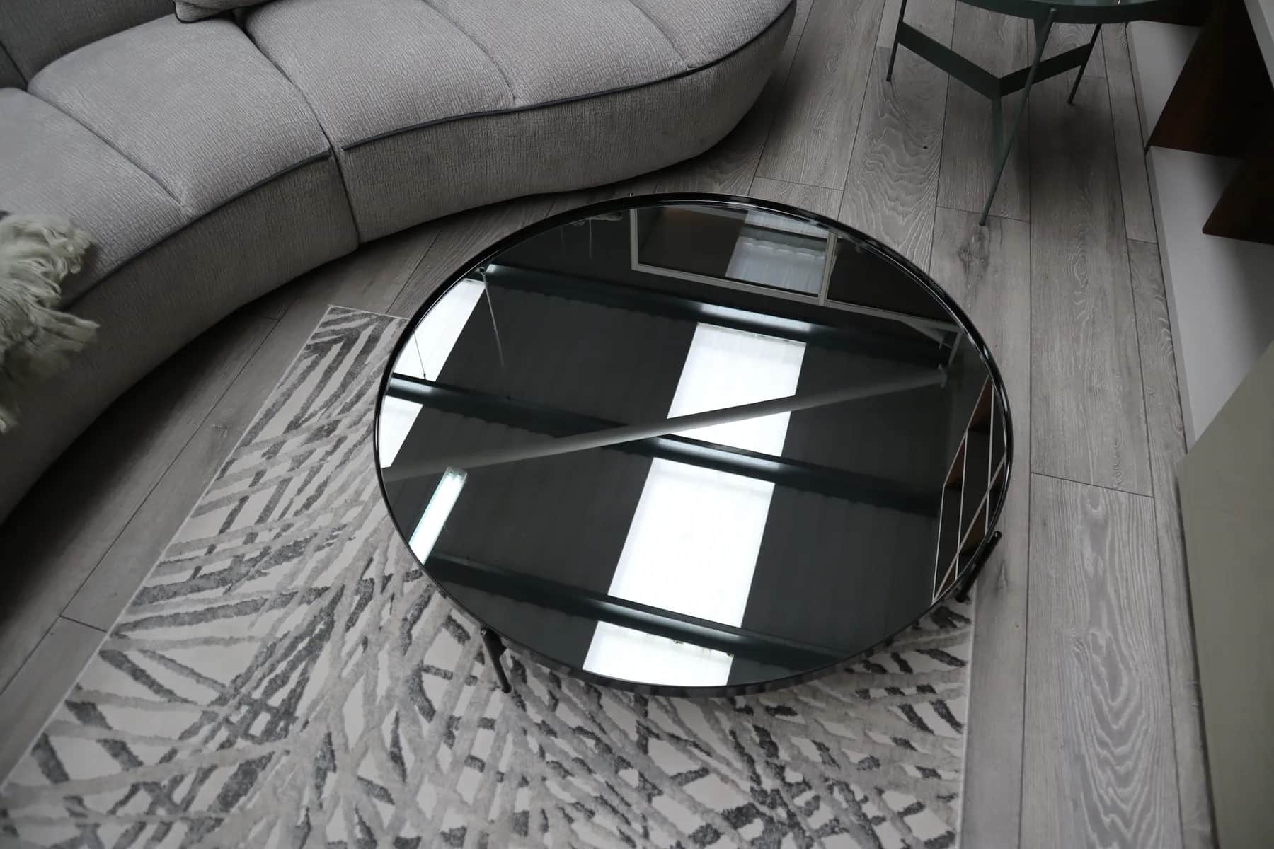 Round black glass coffee table on a patterned rug beside a curved sofa
