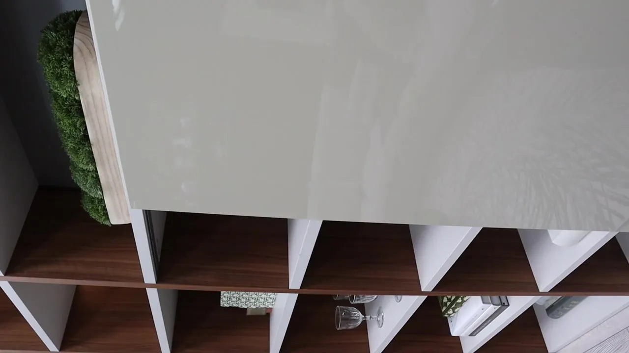 Glossy pale cabinet door above walnut cube shelving with a moss display