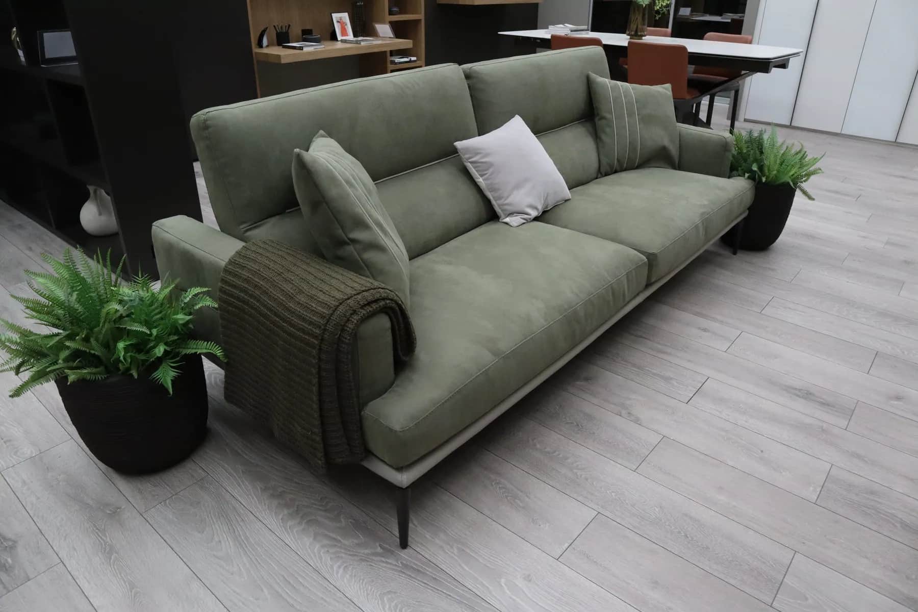 Sage green sofa with cushions and a knitted throw on a wood floor