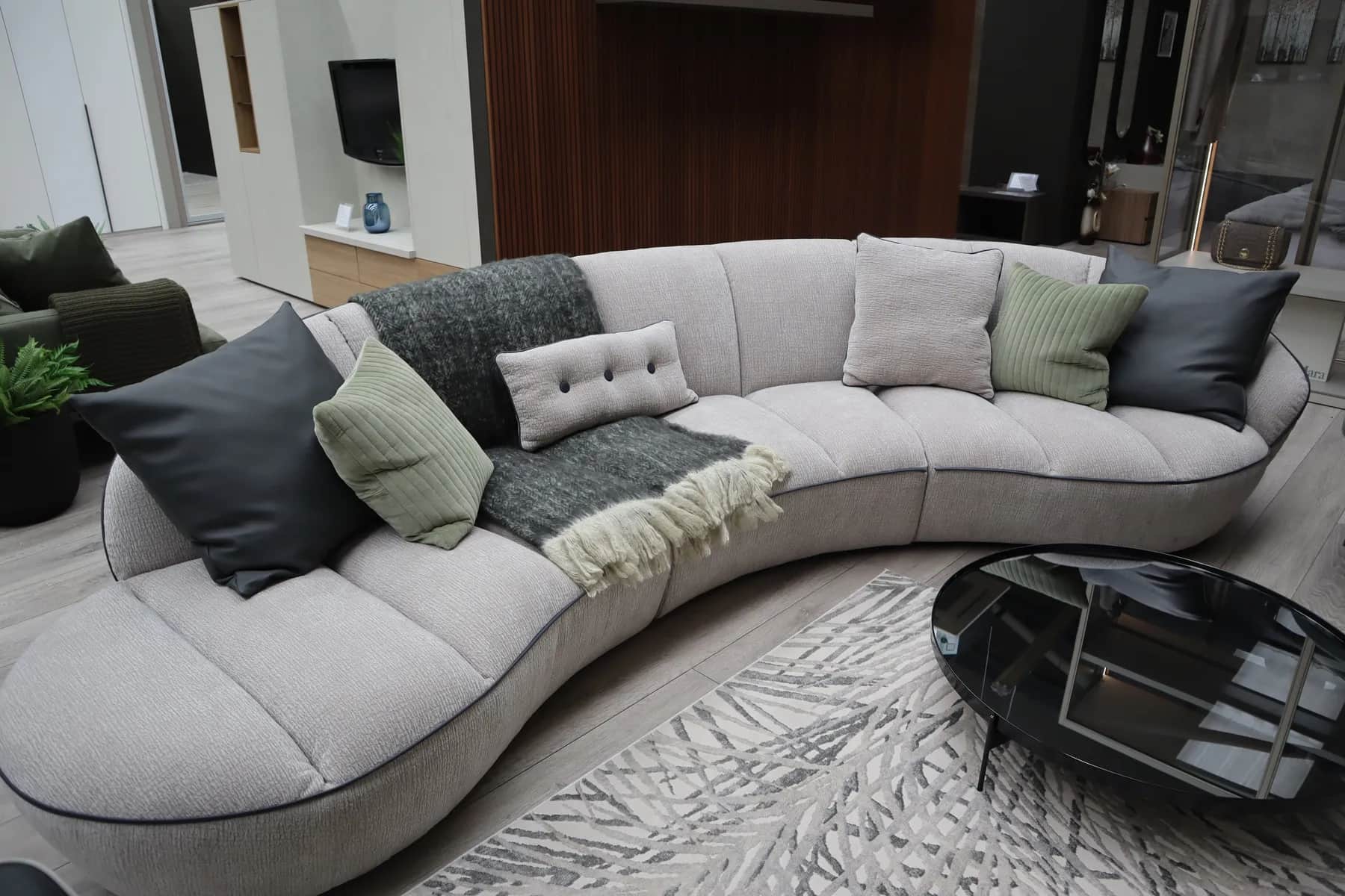 Curved light grey sofa with scatter cushions beside a black glass coffee table