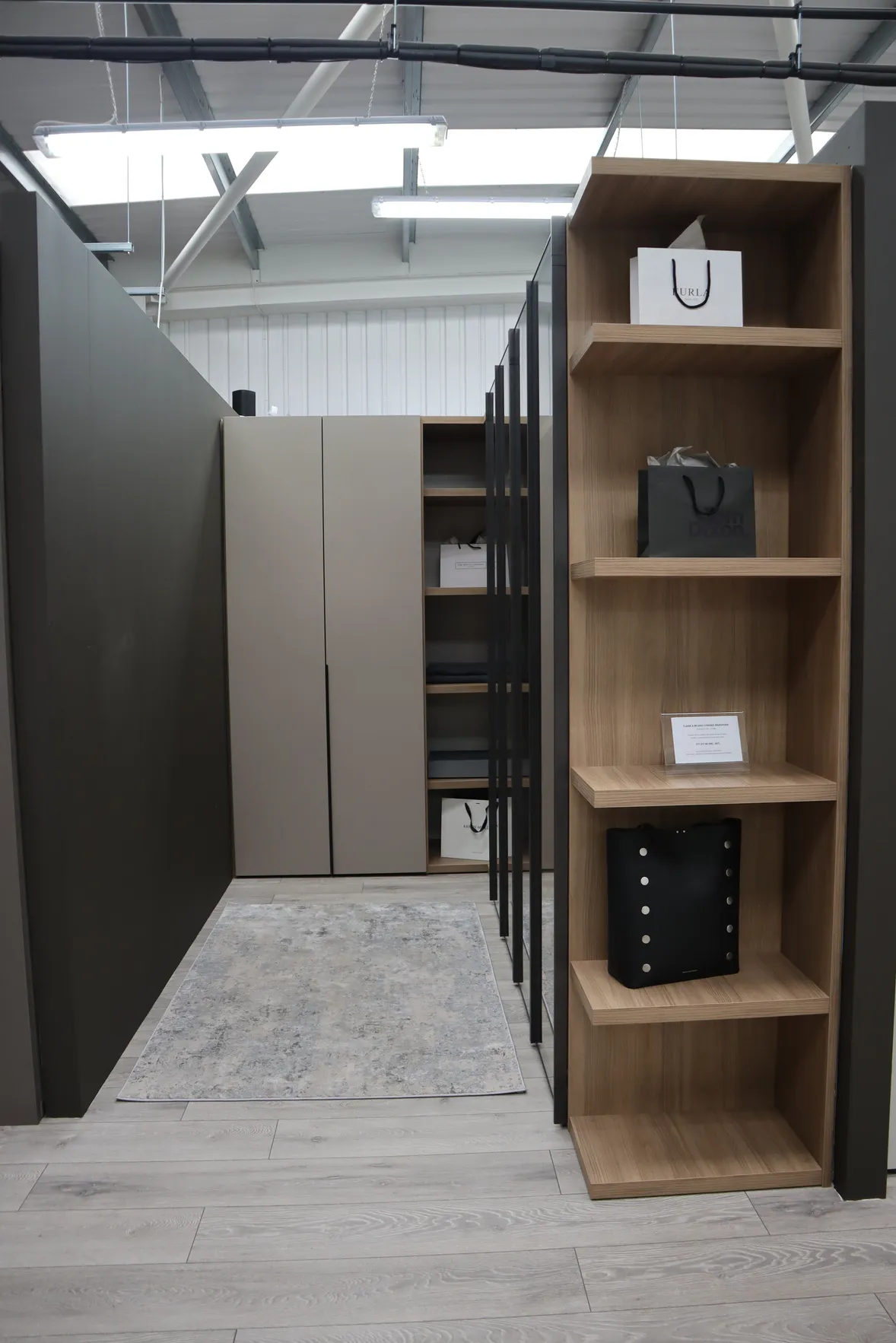 Walk-in wardrobe showroom aisle with oak shelving unit and taupe wardrobe doors