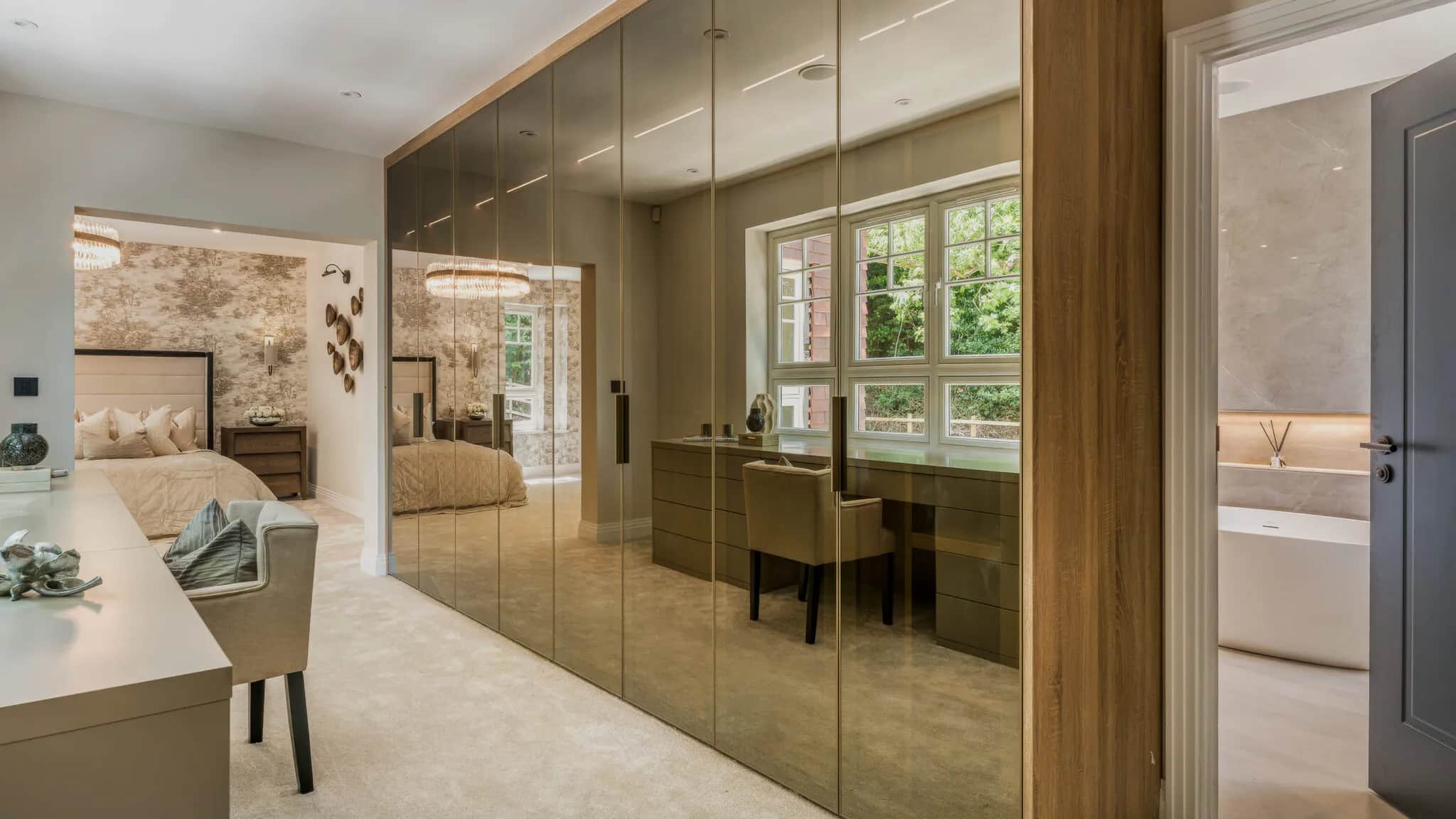 Bronze mirrored fitted wardrobe in a bedroom with desk and en-suite bath beyond