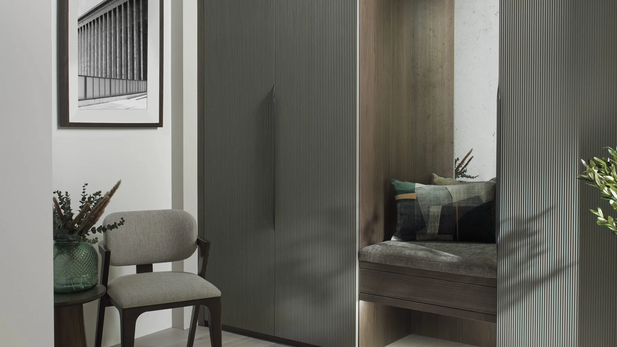 Fluted grey-green wardrobe doors beside a walnut-lined window seat with cushions