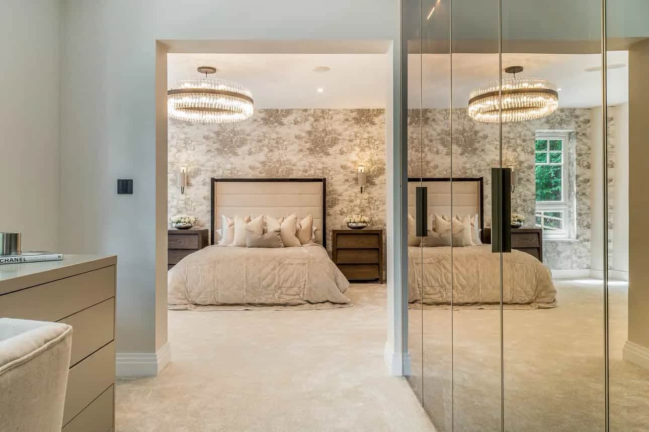 Mirrored wardrobe doors reflecting a luxurious bedroom with chandelier and upholstered bed