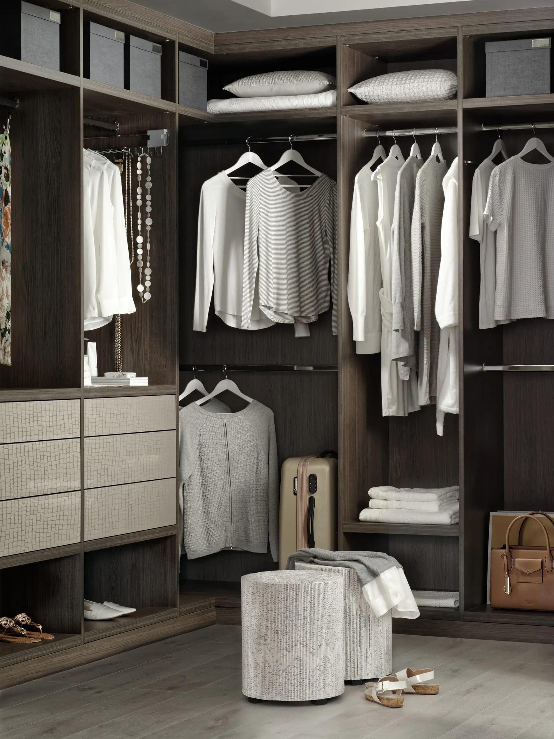 Corner walk-in wardrobe in dark oak with hanging rails, fabric drawers and an upholstered pouffe