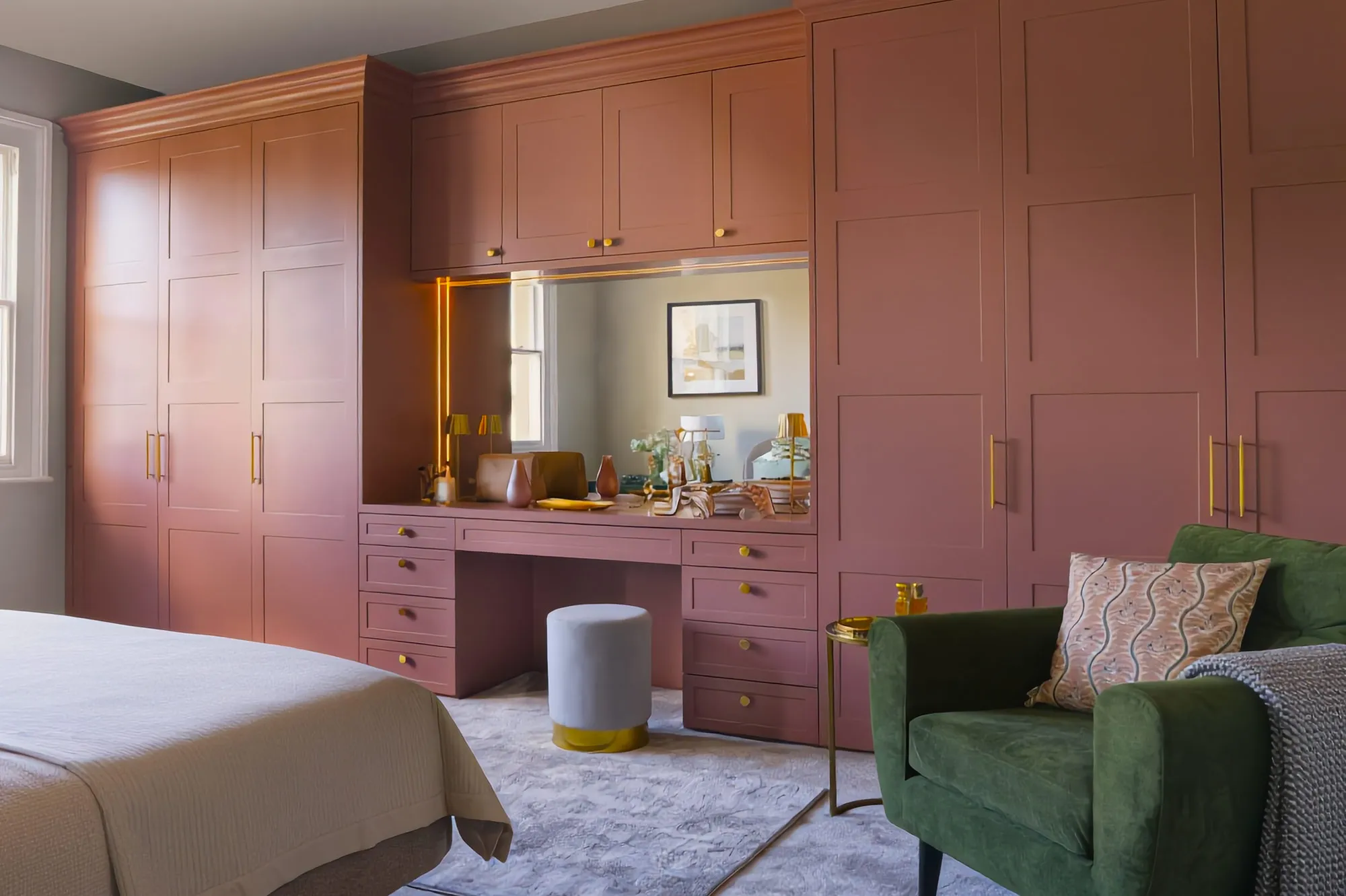 Pink Shaker fitted wardrobes with a built-in dressing table, brass handles and green armchair