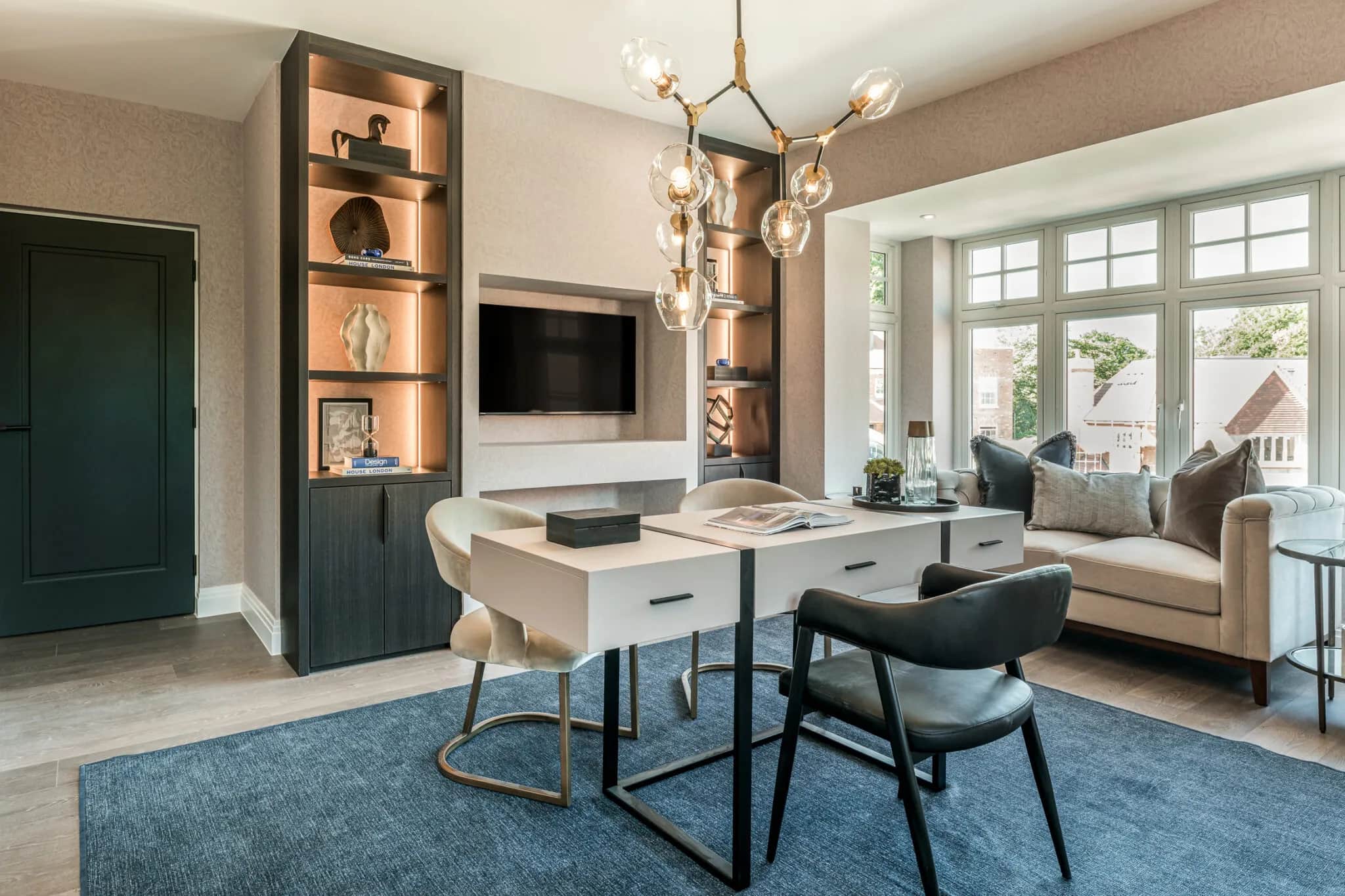 Home office with dark oak shelving unit, wall-mounted TV, white desk and chairs, and bay window seating