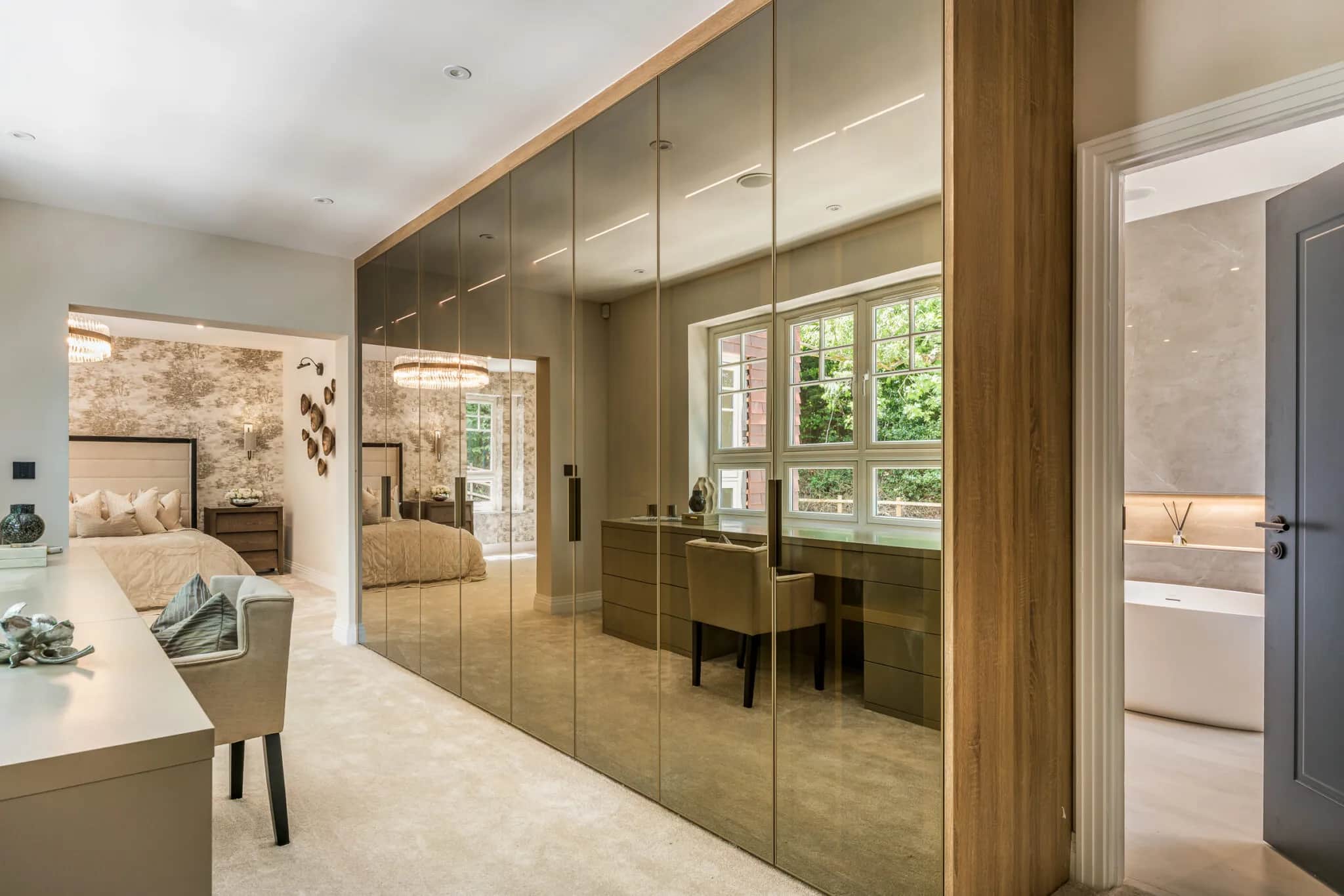 Fitted wardrobes with bronze mirrored glass doors beside a dressing area and en suite