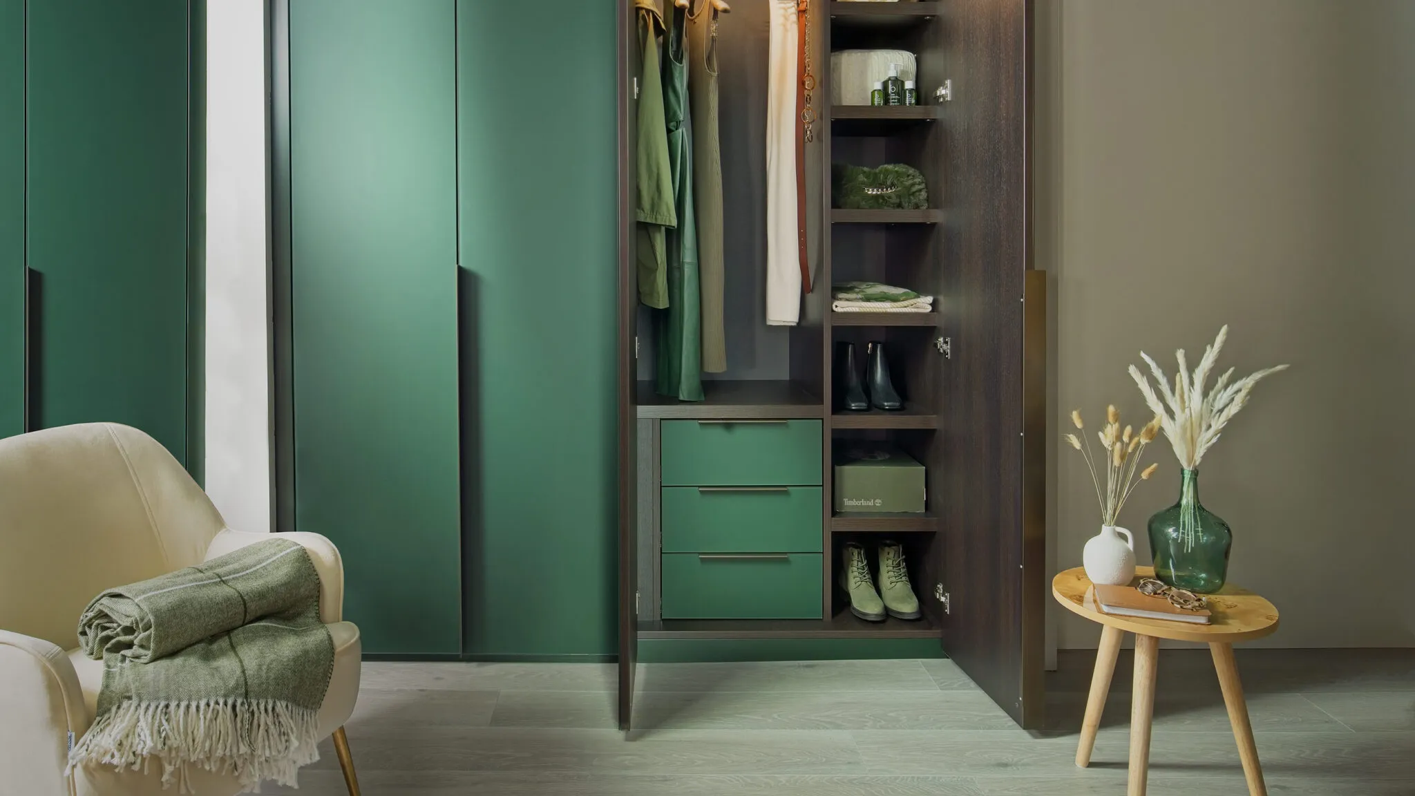 Green fitted wardrobe with one door open showing hanging rail, shelves and green drawers