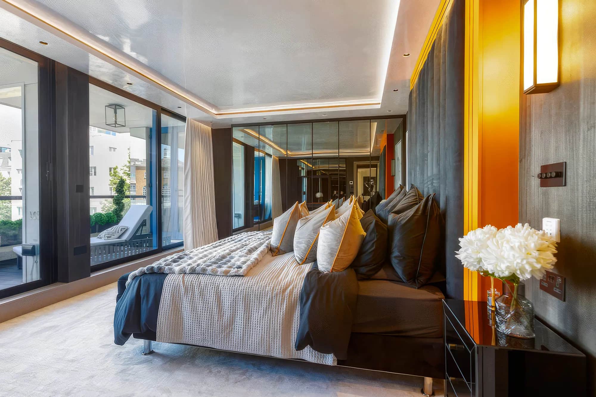Penthouse bedroom with mirrored fitted wardrobes, floor-to-ceiling windows and warm ceiling lighting