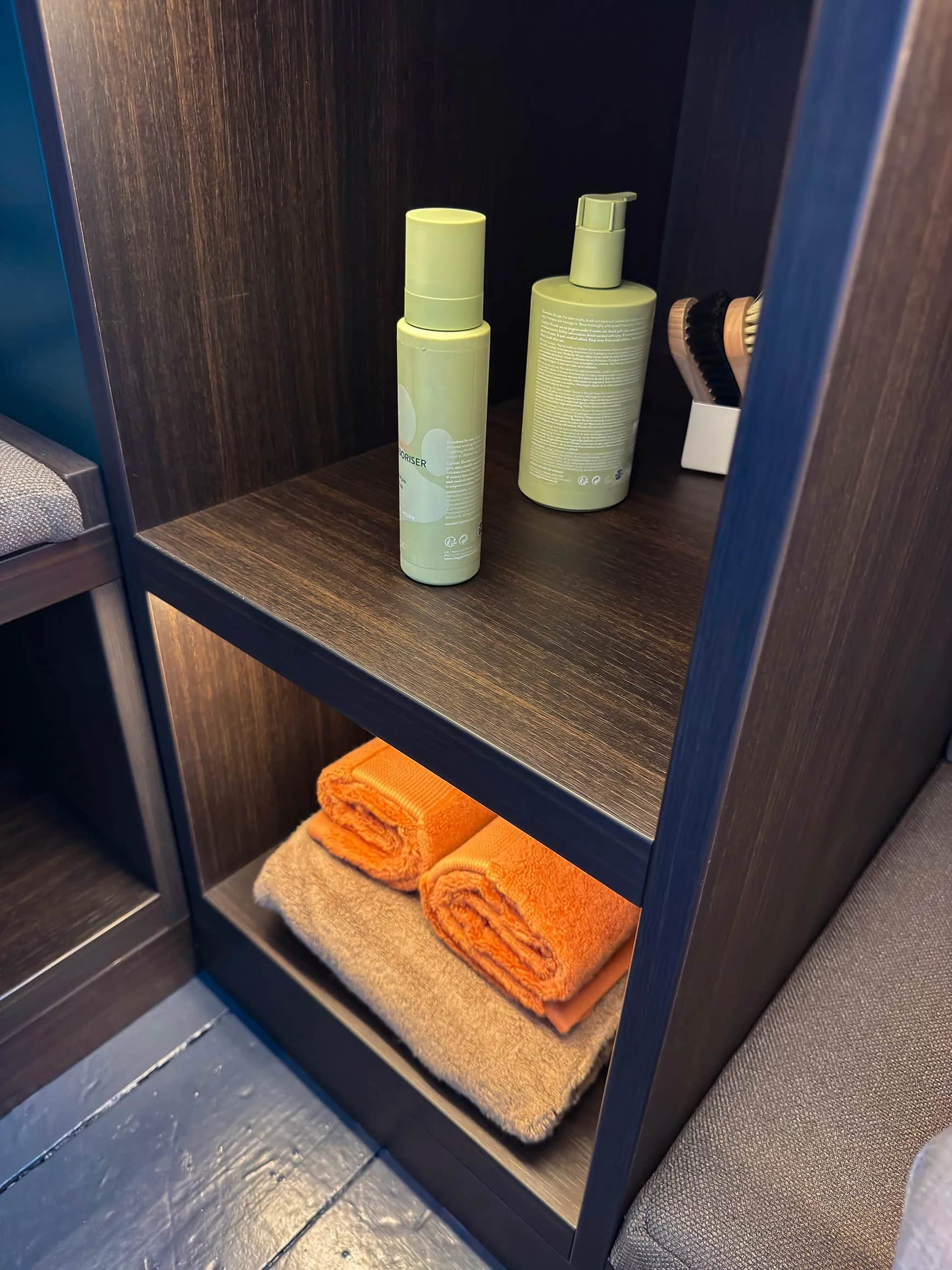 Dark oak boot room shelving with towels, toiletries and open cubbies above a cushioned bench seat